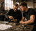 Vater und Sohn in einer kleinen Schlosserei besprechen ein gefrästes Werkstück. Typische Arbeitsumgebung einer kleinen Werkstatt auf der Suche nach der passenden Fräsmaschine.